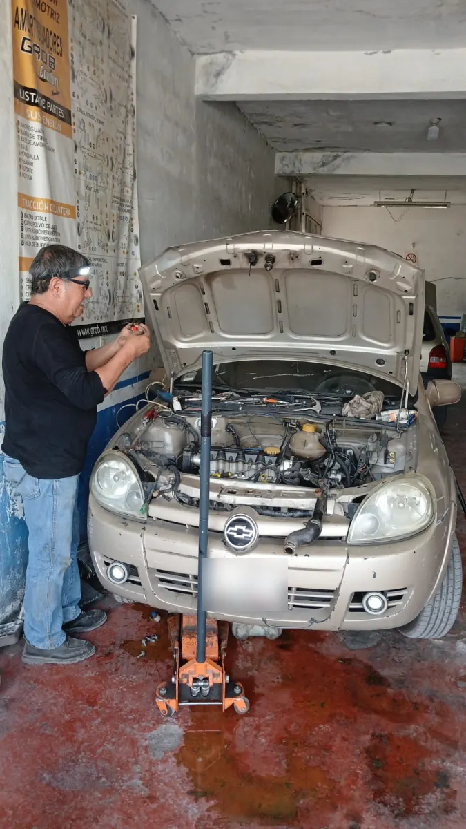 Mecánico de Tajuza revisando el motor de un Chevrolet con el cofre abierto y el gato hidráulico puesto